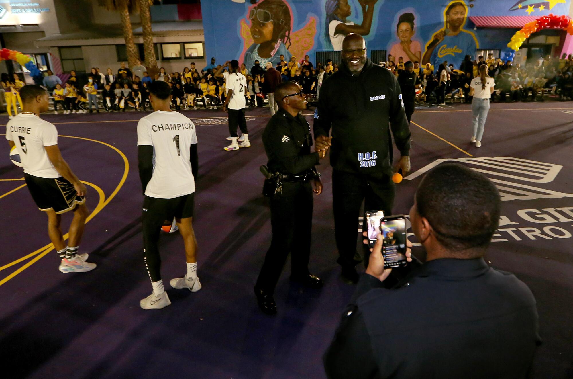Shaquille O'Neal poses for photos at the Challengers Boys & Girls Club while shaking hands with a police officer.