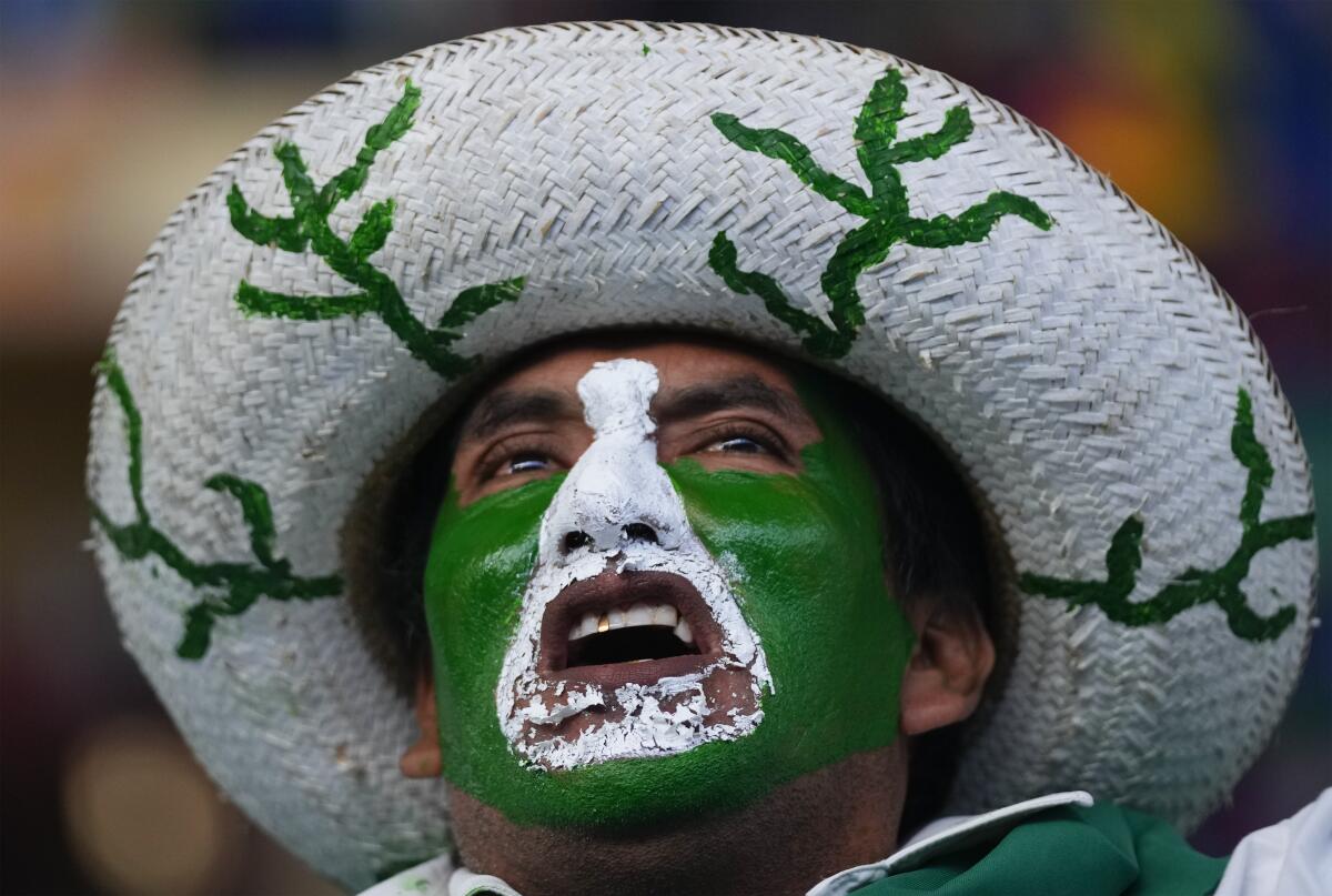 A person with face painted green and white wears a white hat with a rim with green plants painted on it