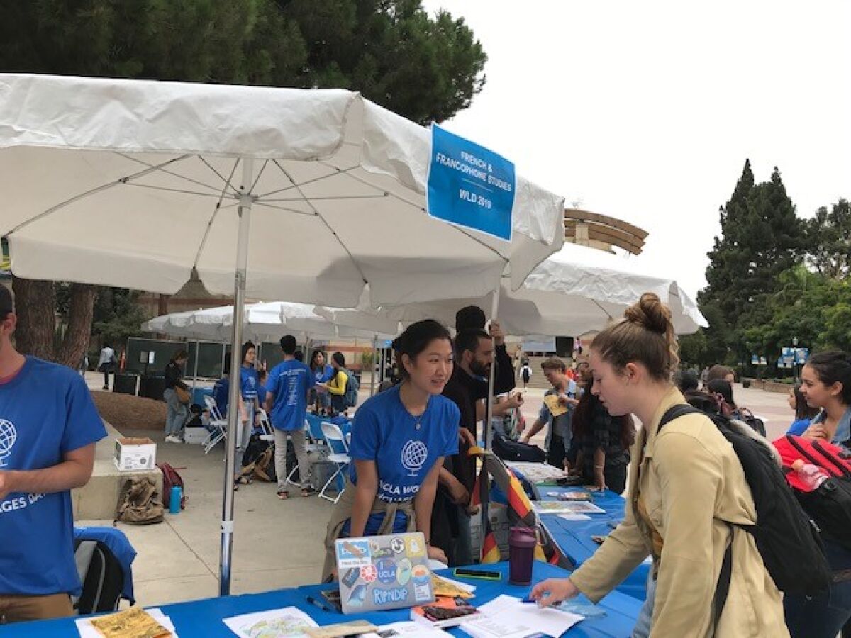 Students in blue shirts speak to other students and hand out fliers at a campus event