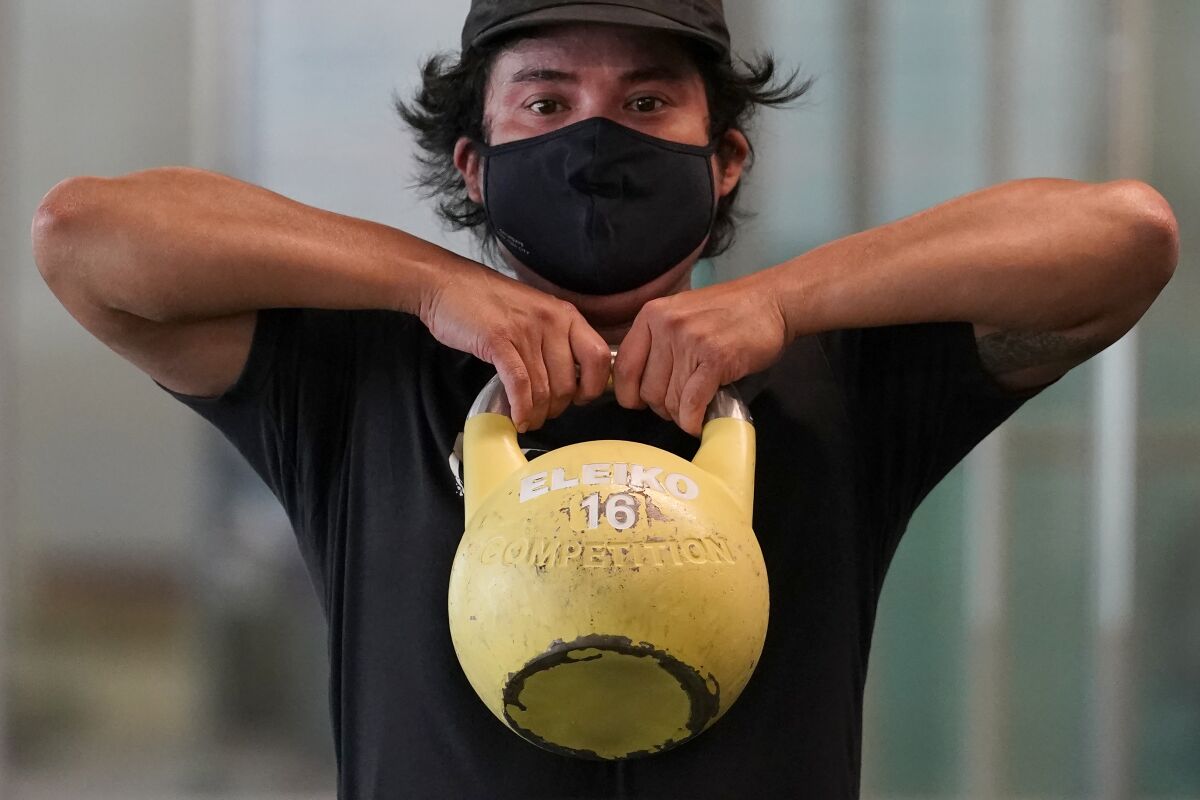 Tim Robles wears a mask while lifting a kettlebell during a workout at Fitness SF Transbay gym.