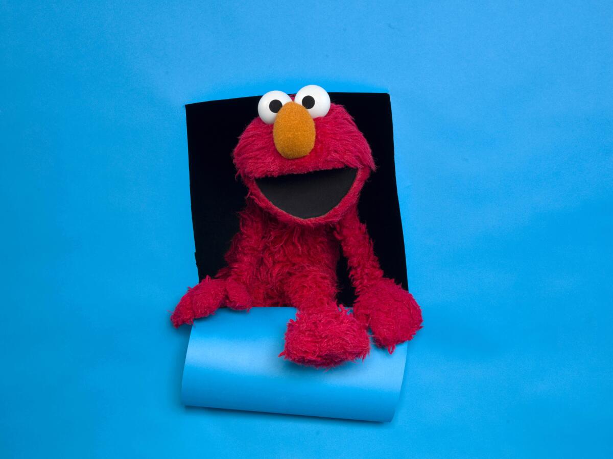 A red Elmo puppet posing against a blue background