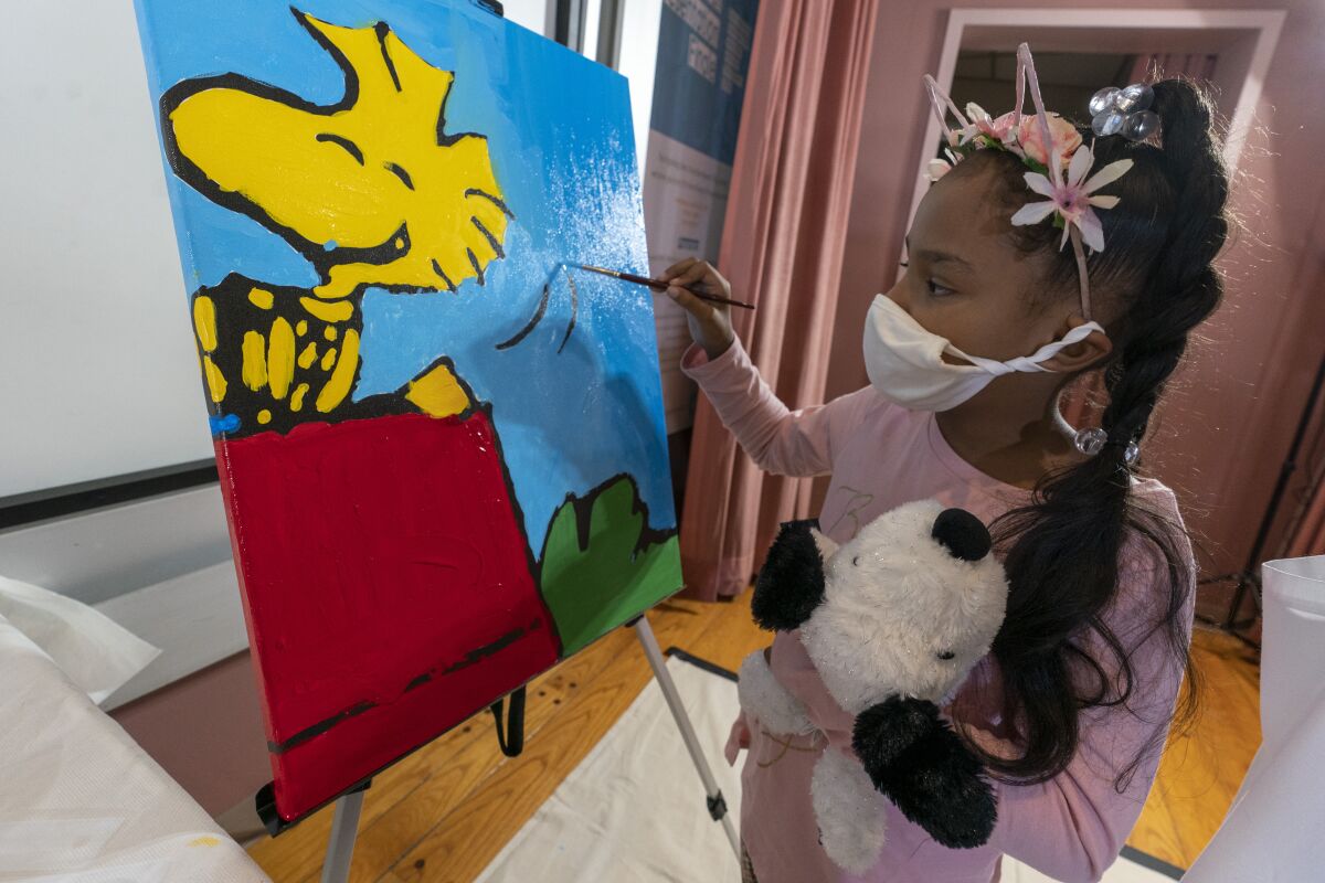 Kaley Williams, 8, paints a panel of a "Peanuts" mural that will be placed in the outpatient pediatric floor of One Brooklyn Health at Brookdale Hospital, Thursday, Oct. 1, 2020, in the Brooklyn borough of New York. The virus pandemic won't stop Charlie Brown, Snoopy or the "Peanuts" gang from marking an important birthday and they're hoping to raise the spirits of sick kids while they celebrate. The beloved comic marks its 70th anniversary this week with new lesson plans, a new TV show and a philanthropic push that includes donating "Peanuts" murals for kids to paint in 70 children's hospitals around the globe, from Brooklyn to Brazil. (AP Photo/Mary Altaffer)