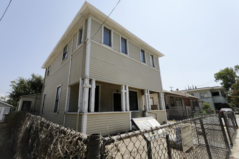 The modest two-story Harada House, surrounded by a chain-link fence.