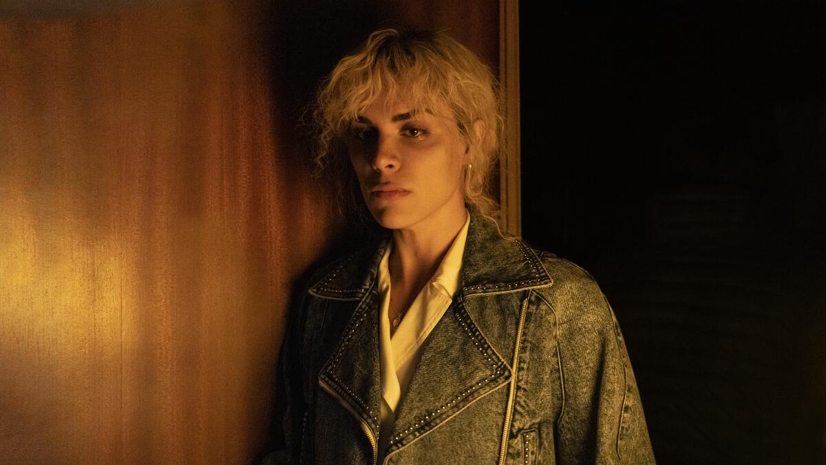 Jedet, as La Veneno, is shown in a denim jacket in soft lighting against a wood wall