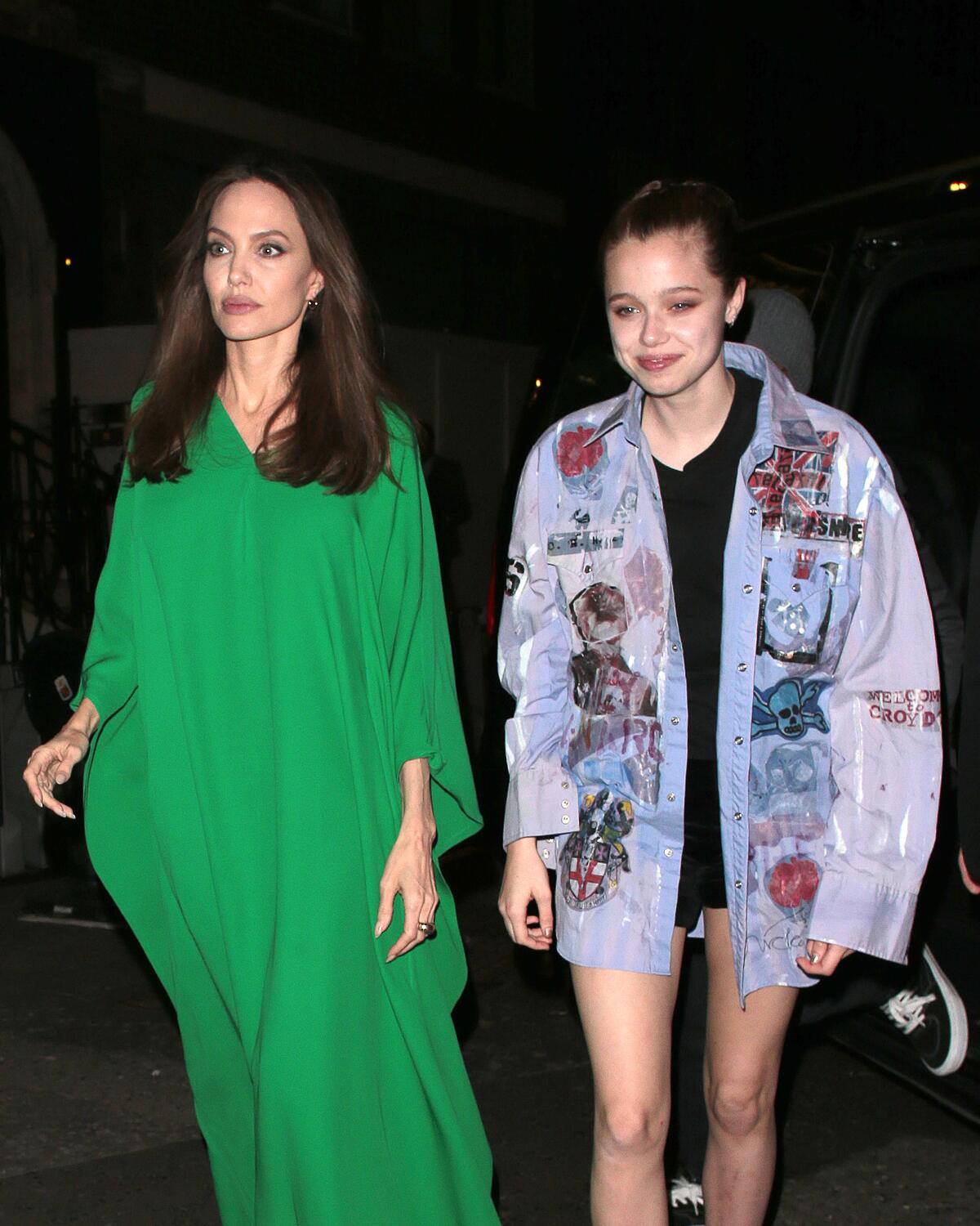 Angelina Jolie walks in a long green gown at night next to daughter Shiloh, who hears a patchwork overshirt