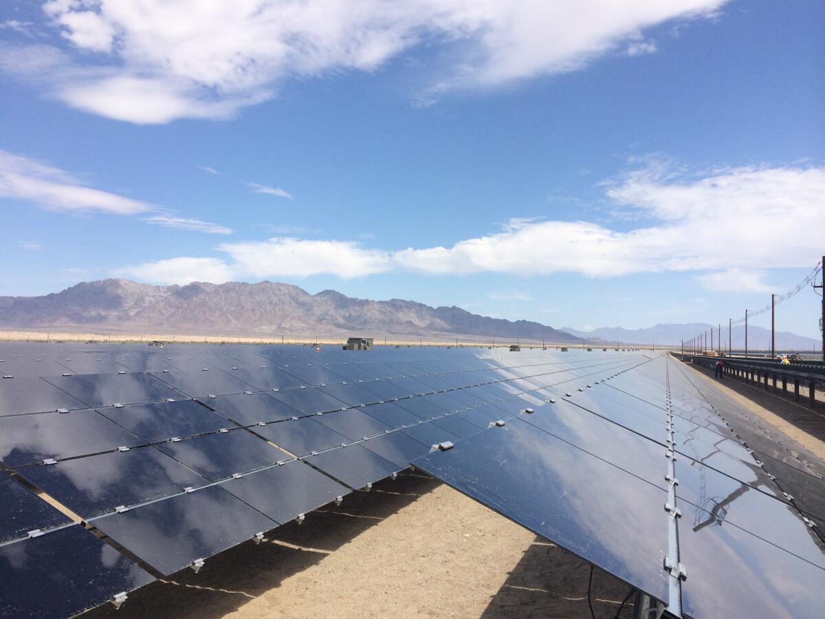 Solar panels in the desert with mountains and blue sky in the background