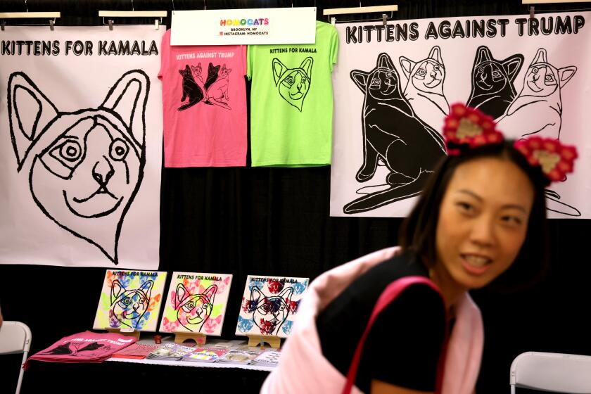 PASADENA, CA - AUGUST 3, 2024 - Karen Lee looks over merchandise that make a political statement in behalf of cats at the Homocats booth at CatCon held at the Pasadena Civic Auditorium in Pasadena on August 3, 2024. The event, often dubbed the comic con for cat lovers, will include cat celebrities, an art show and all things cat related. The event comes days after 2021 Fox News interview of Republican vice presidential nominee Sen. J.D. Vance's surfaced in which he complains that the country was being run by Democrats, corporate oligarchs and "a bunch of childless cat ladies who are miserable at their own lives and the choices that they've made and so they want to make the rest of the country miserable, too." (Genaro Molina/Los Angeles Times)