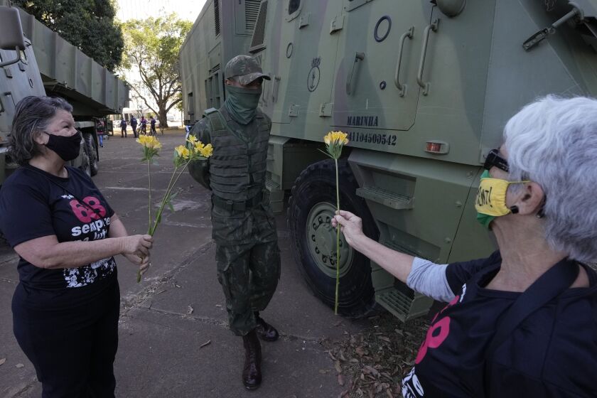 Women offer flowers to a soldier in a show of opposition to Brazilian President Jair Bolsonaro after a military convoy passed Planalto presidential palace and parked outside the Navy headquarters in Brasilia, Brazil, Tuesday, Aug. 10, 2021. The convoy paraded by the palace on Tuesday, the day of a key congressional vote on a constitutional reform proposal supported by Bolsonaro that would add printed receipts to some of the nation’s electronic ballot boxes. (AP Photo/Eraldo Peres)