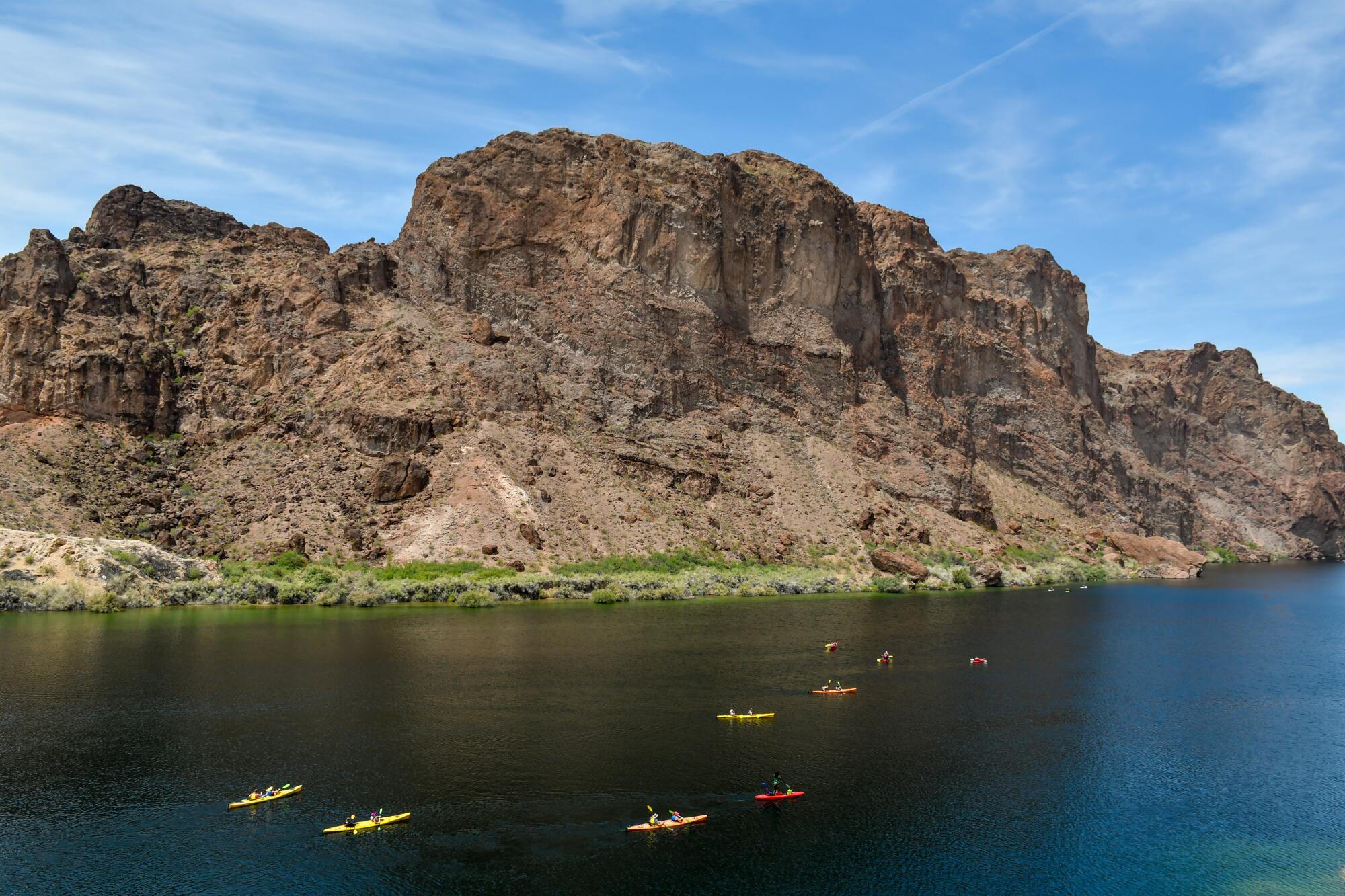 Mountain buttes rise above kayaks floating in the Colorado River