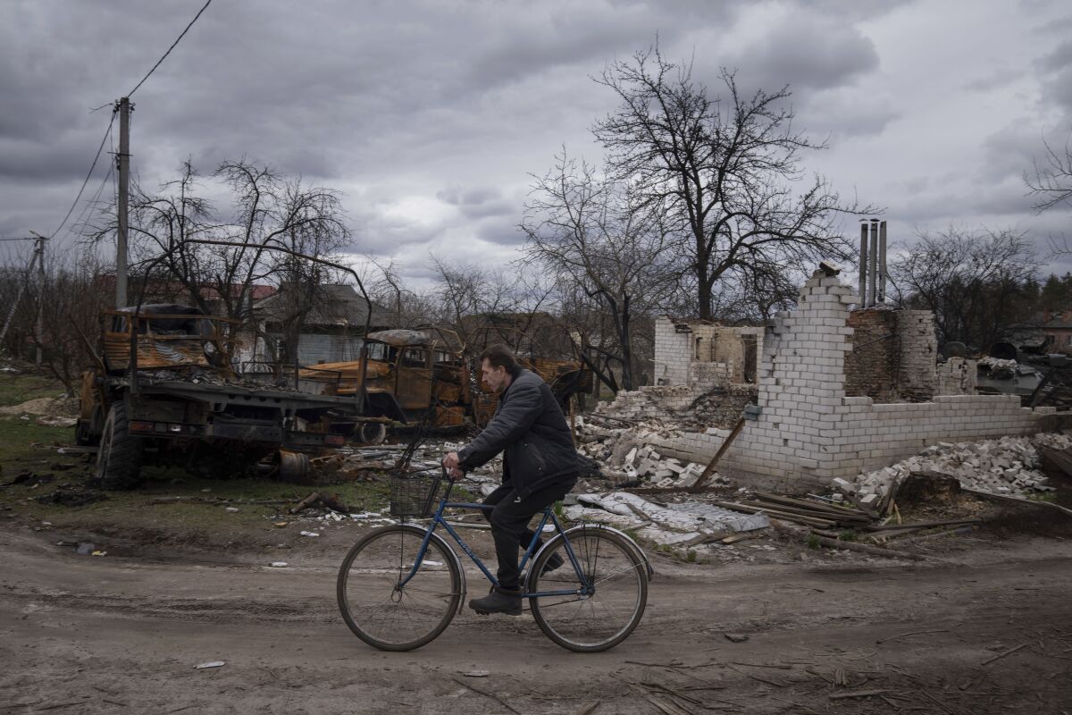A man rides a bicycle past destroyed vehicles and an apartment building in Yahidne, near of Dnipro, Ukraine, Tuesday, April 12, 2022. (AP Photo/Evgeniy Maloletka)