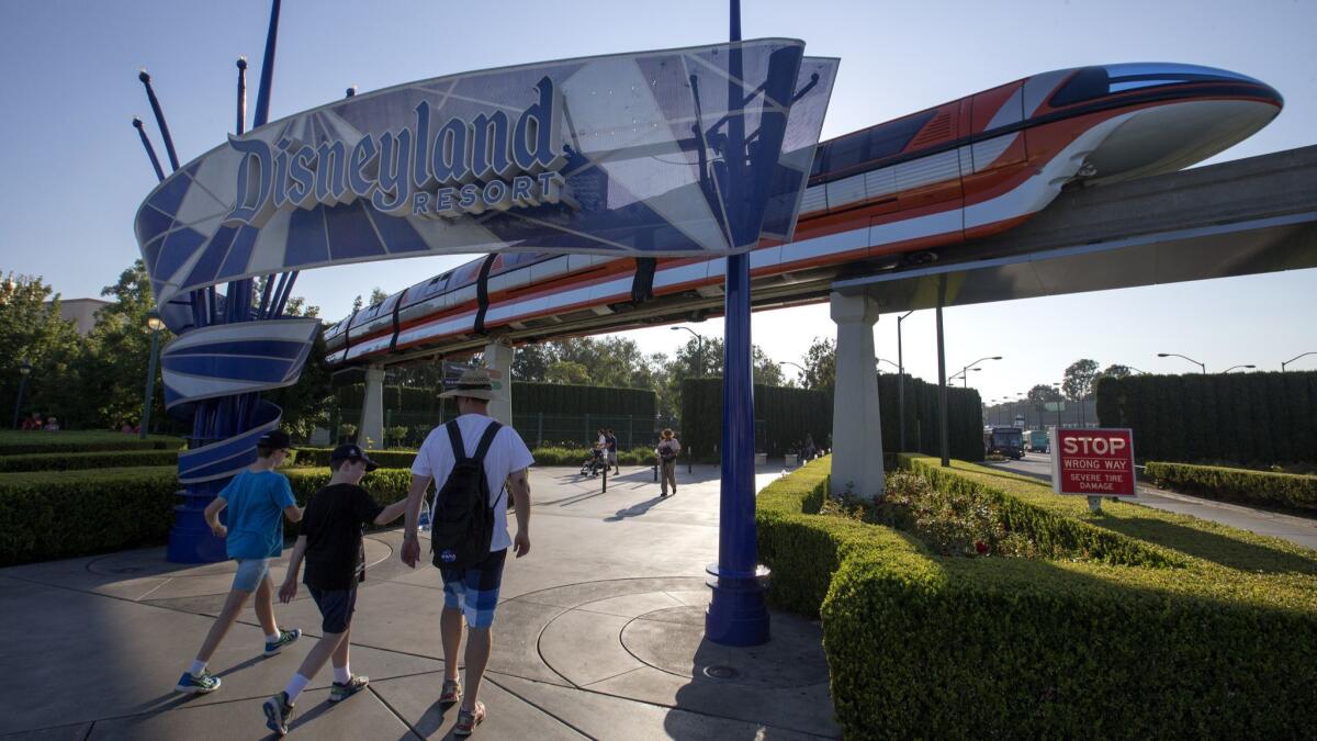 The Disneyland Monorail passes by as people walk under the Disneyland sign in Anaheim. A campaign for a living wage measure in Anaheim has drawn huge donations from unions and the Walt Disney Co. The two sides dispute whether the measure applies to the resort.