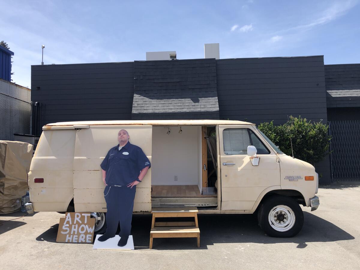 A profile shot of a white delivery van includes a cardboard cut-out of a guard and a sign that says "Art Show Here"
