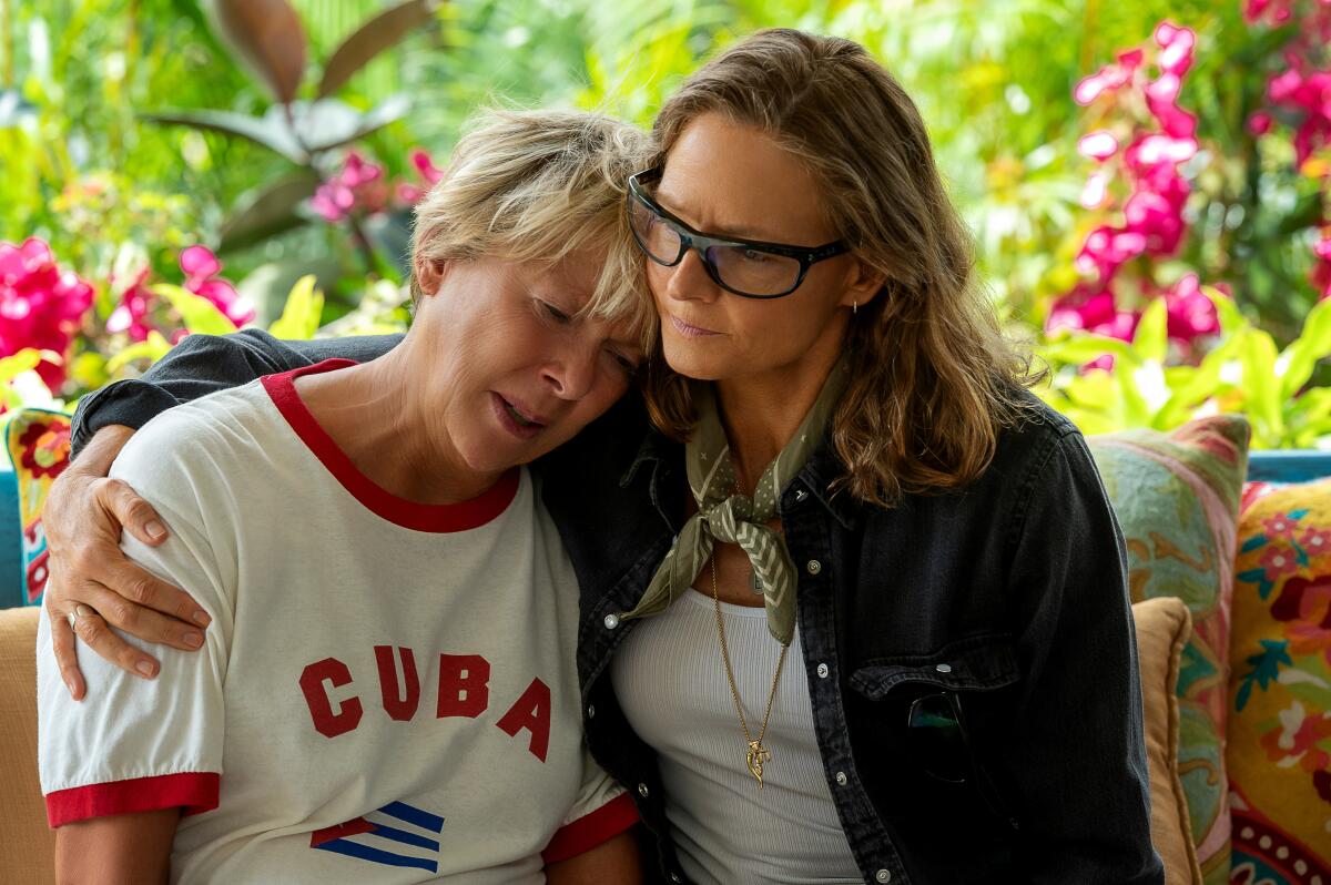 A woman consoles a woman in a Cuba T-shirt who's crying, putting an arm around her shoulder.
