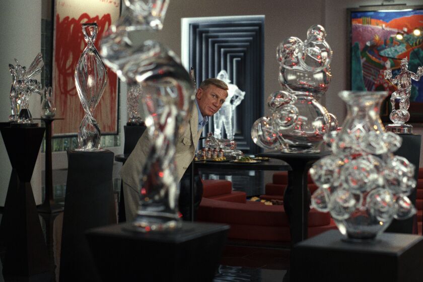 A man in a beige suit surrounded by a bunch of glass statues on pedestals
