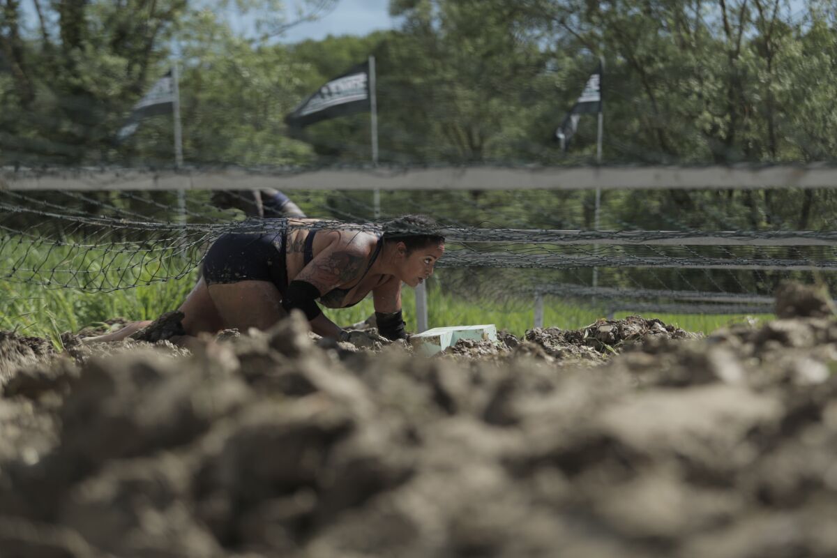 A woman crawls under razor wire through the dirt