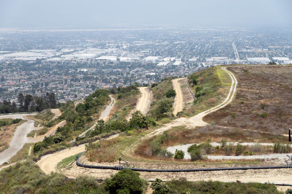 An aerial view reveals terraces carved into a scrubby hilltop. The San Gabriel Valley is visible in the distance.