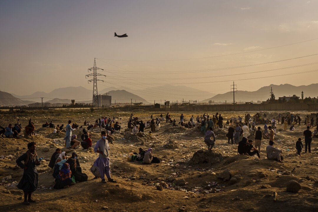 A military transport plane takes off while Afghans watch and wonder while stranded outside.