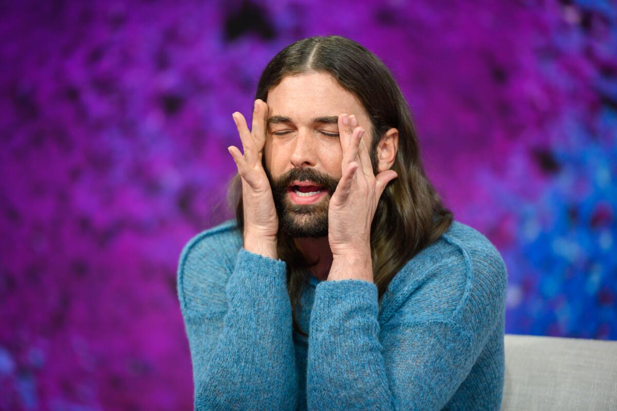 Jonathan Van Ness holding their face with eyes closed while wearing a turquoise blue sweater