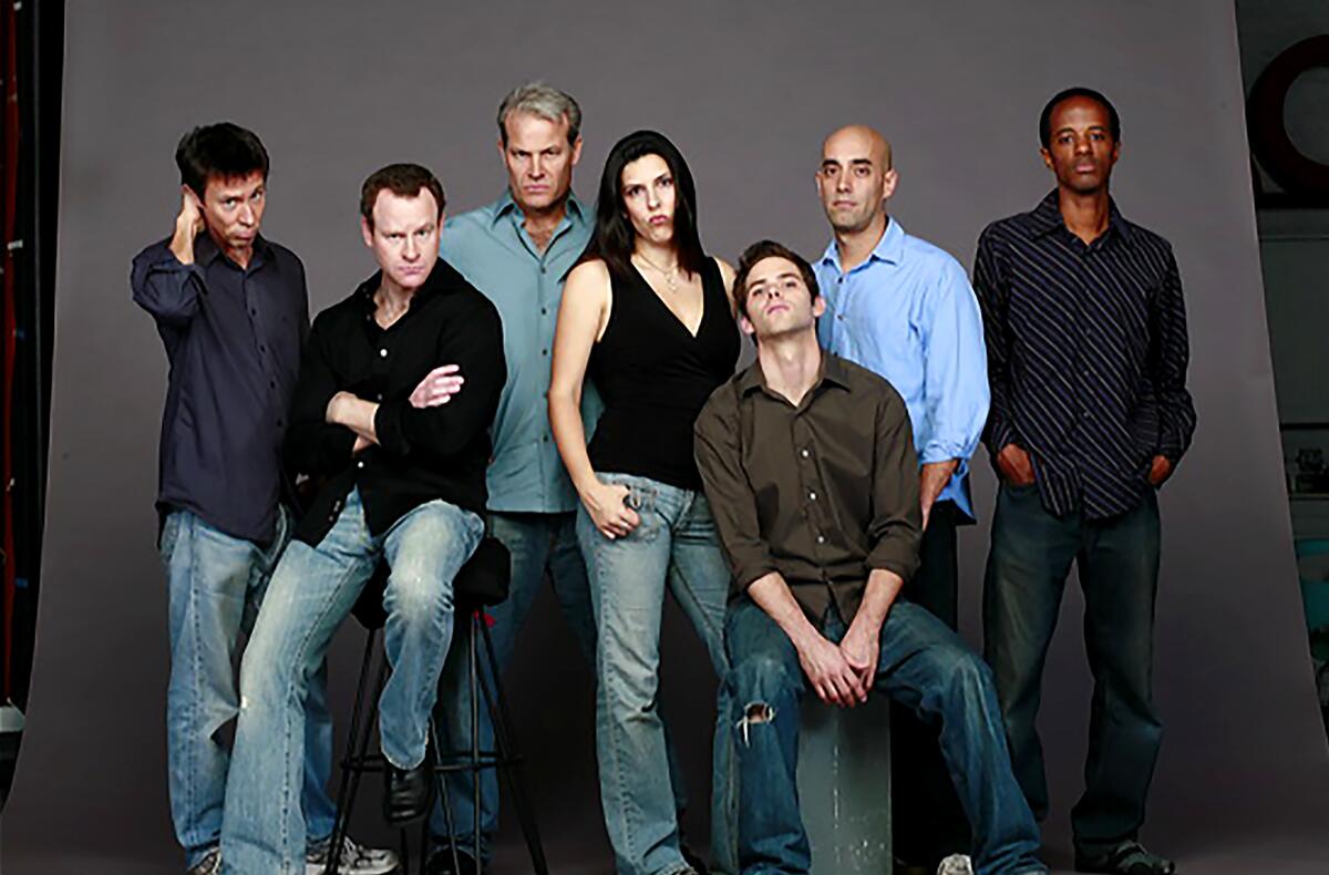 A group of men and a woman sitting and standing while posing for a photo.