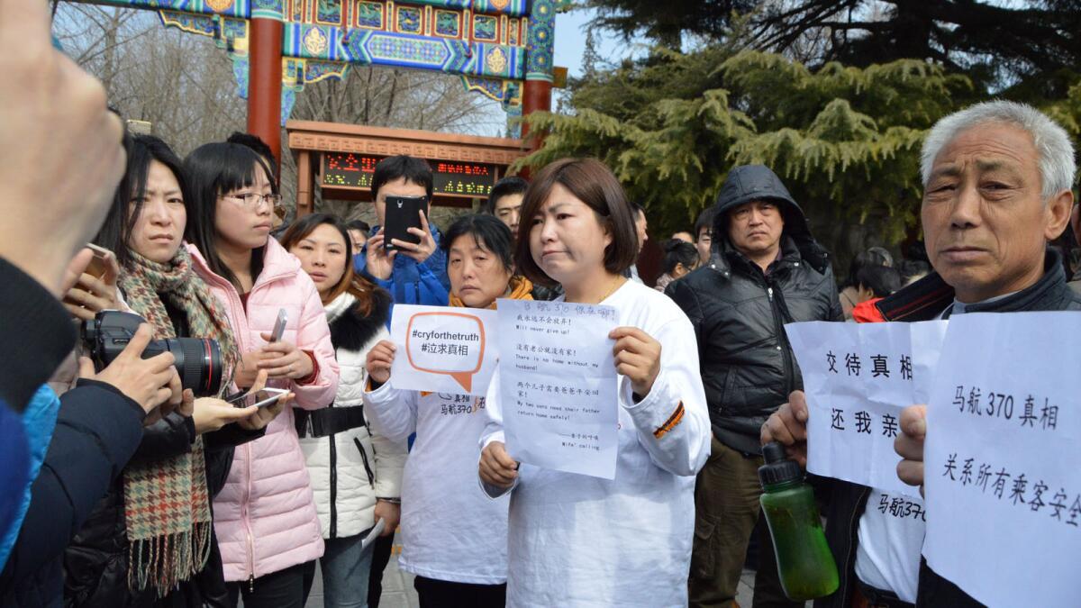 Cheng Liping, center, holds up a sign begging for information on the whereabouts of her husband, who was aboard Malaysia Airlines Flight 370, at a memorial service in Beijing.