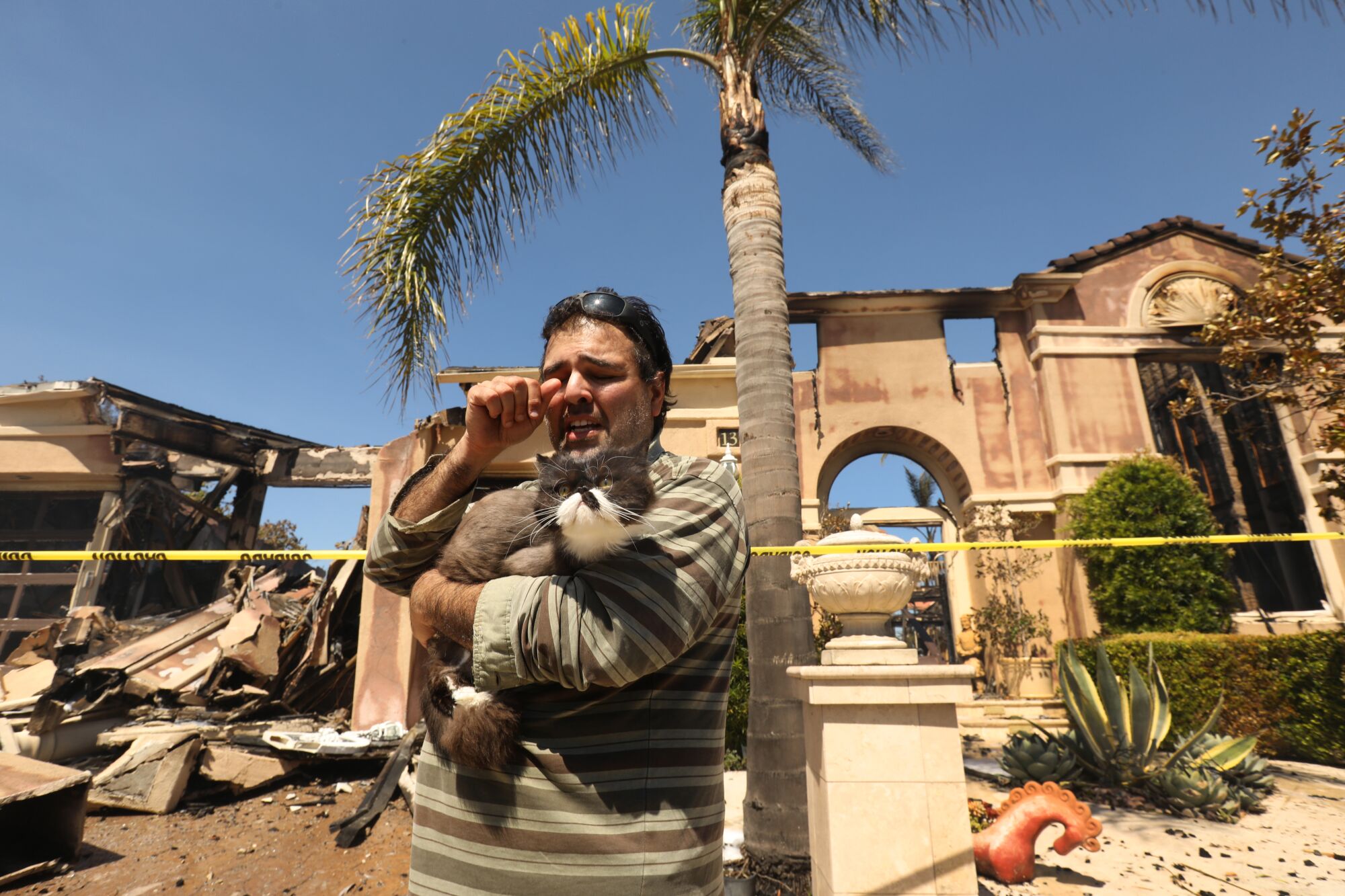 Sassan Darian holds his cat as he assesses the damage outside his father's home 