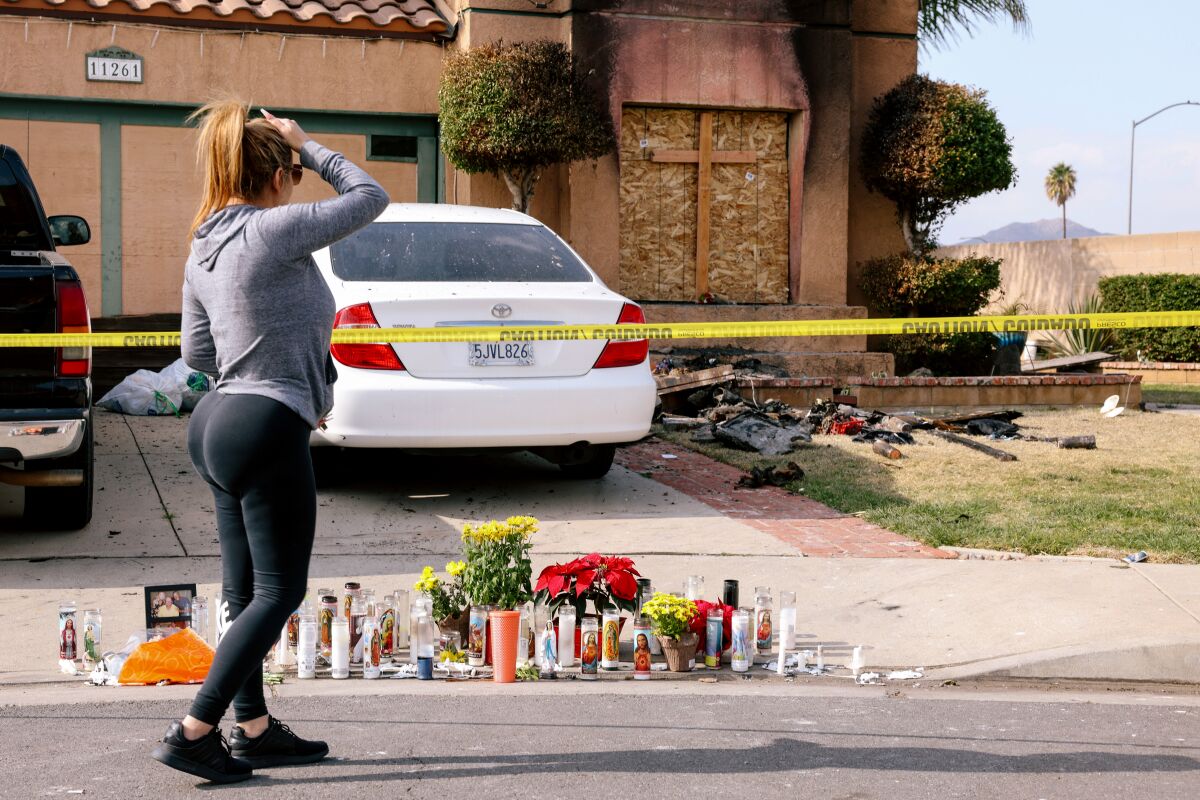A woman looks at a memorial outside a home where the deaths of three people were found Friday