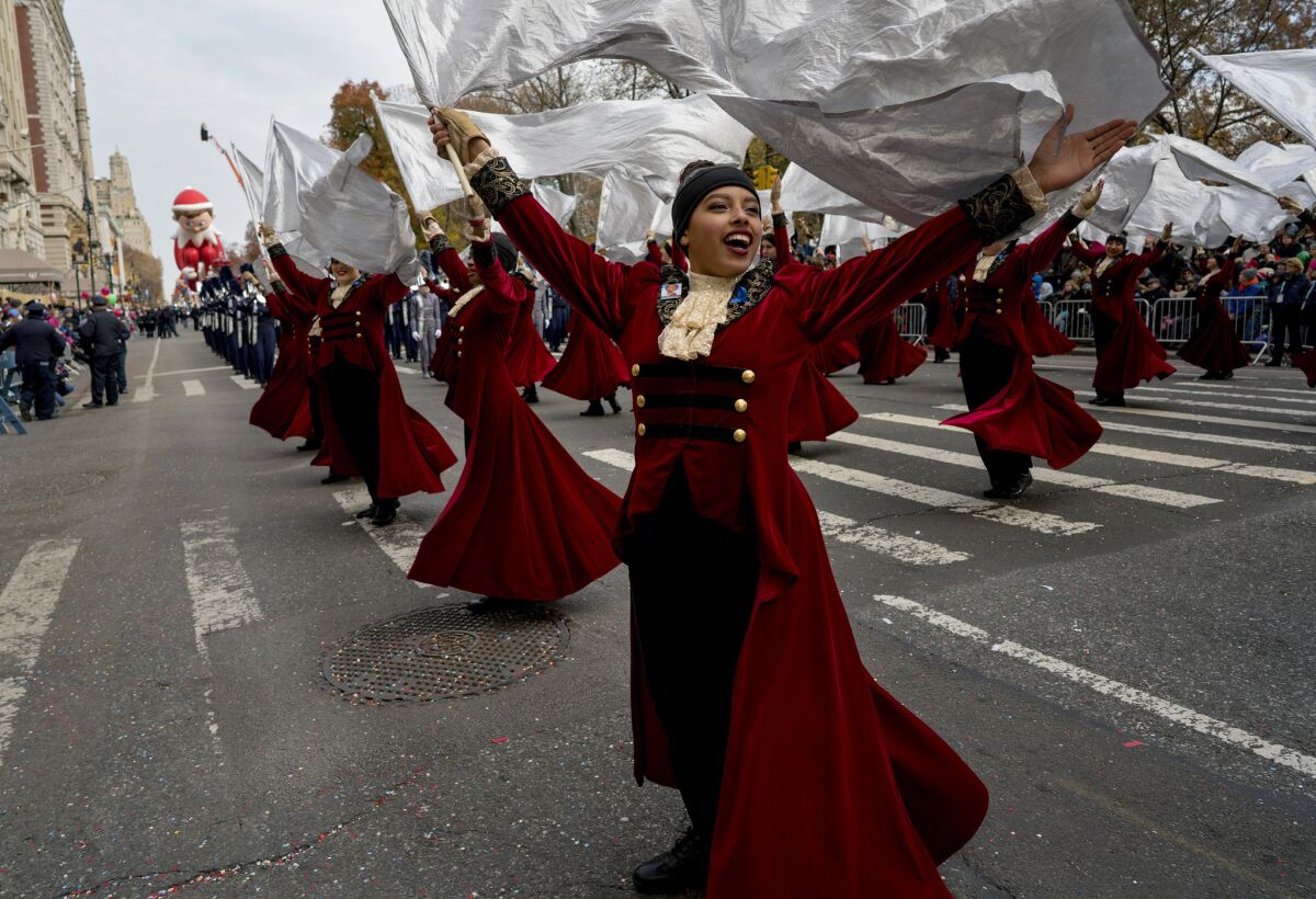 High school band members, in costumes of swirling robes and lace jabots, carry streaming white flags.