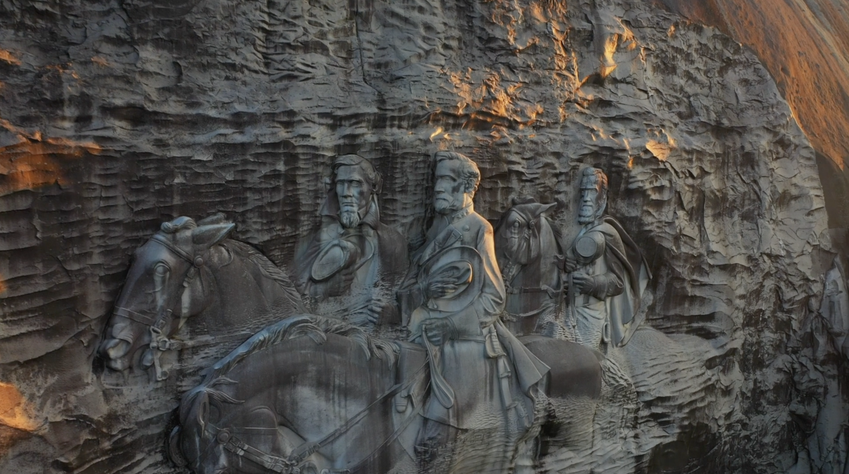 A drone's eye view of a towering rock facade bears bas relief carving of Confederate leaders on horseback.