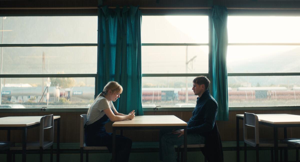 Two people sit at a table against windows in the movie "The Night of the 12th."