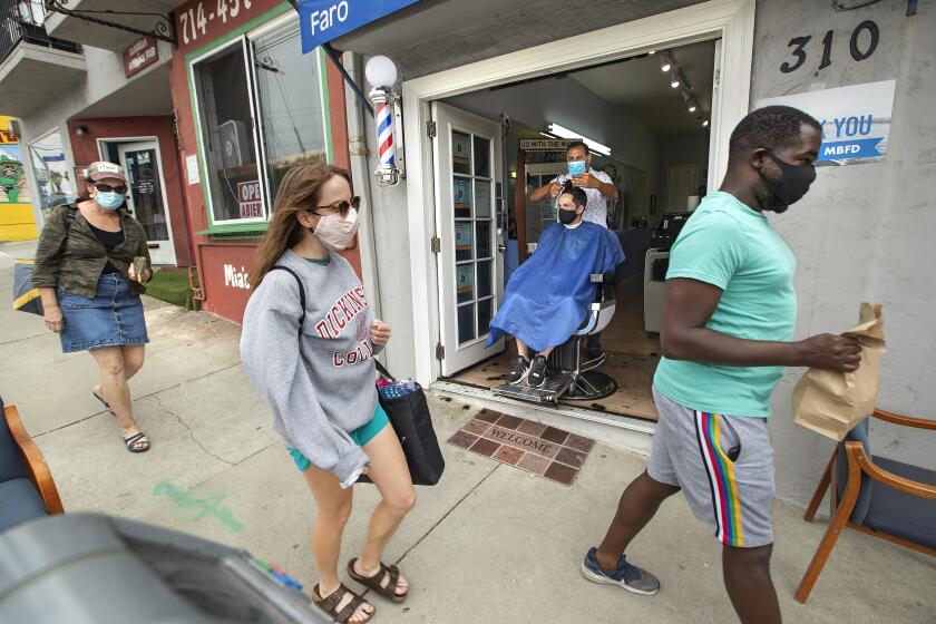 MANHATTEN BEACH, CA -JULY 29, 2020: Faro Tabaja, owner of Waves Barbershop & Boutique on Rosecrans Ave. in Manhattan Beach, gives a haircut to Gene Geiser of Manhattan Beach. Tabaja moved the barber's chair into the entry way to create a safer environment to cut hair due to the coronavirus outbreak. (Mel Melcon / Los Angeles Times)