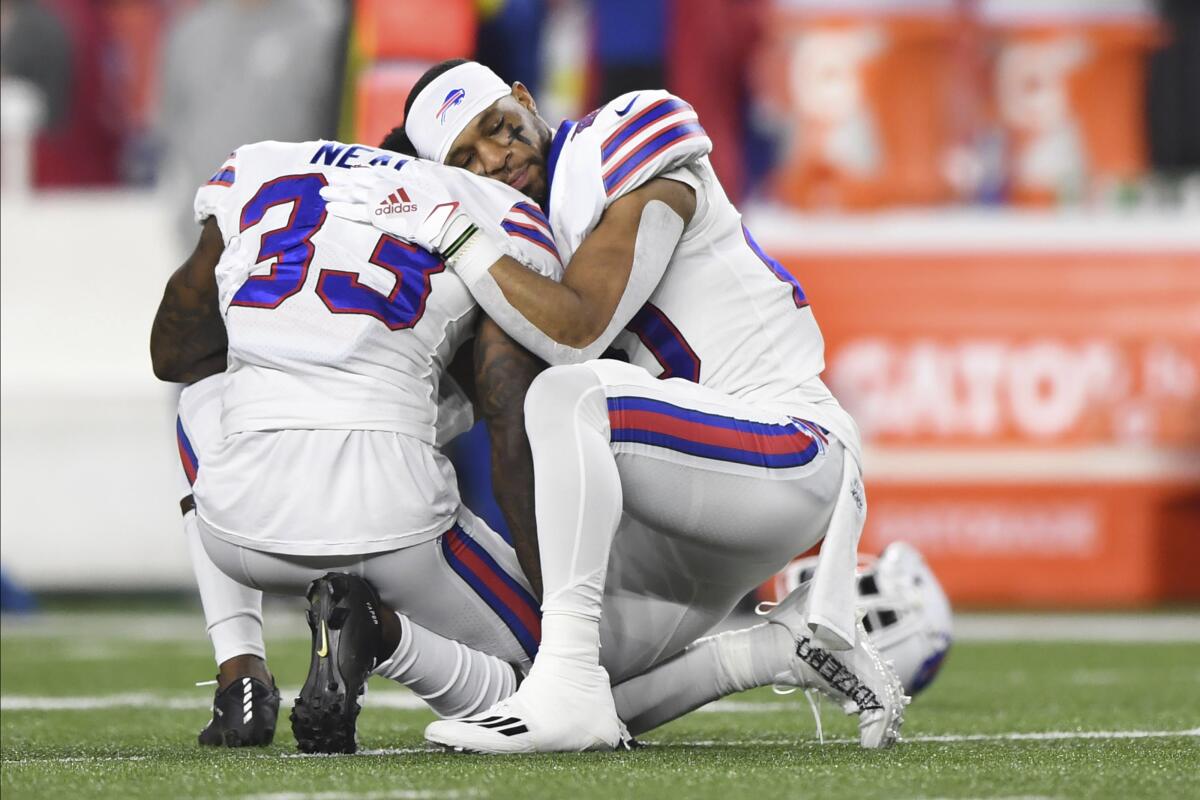 Two football players kneel and embrace on the field.