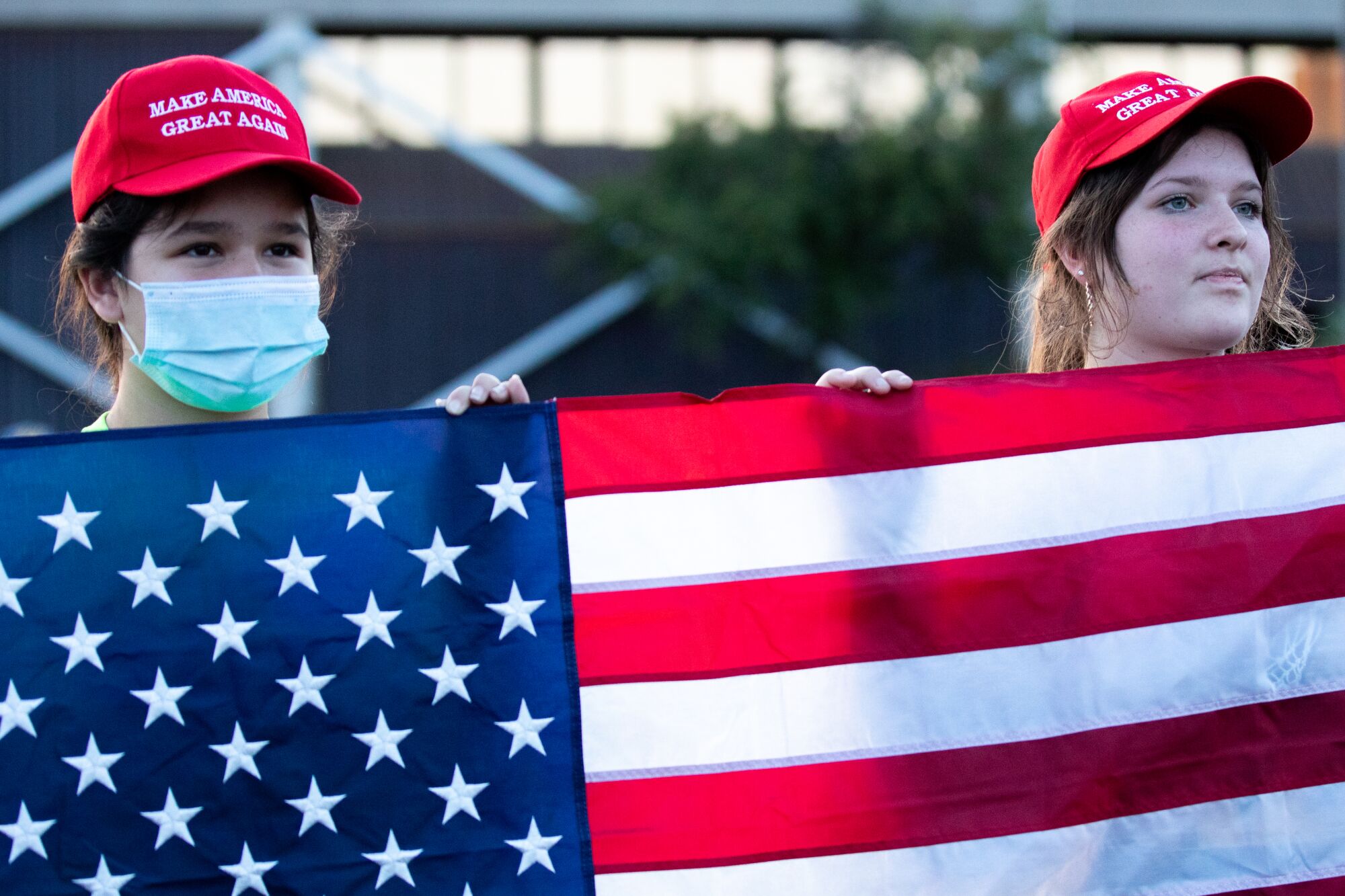 Two young people wearing red Make America Great Again hats hold up a U.S. flag

