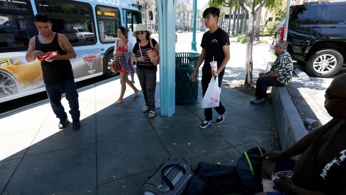 Victor Gutierrez, 43, left, who is homeless and sleeps in his automobile, hangs out under a bus shelter while people board and exit an Orange County Transit Authority bus at the corner of Harbor Boulevard and Katella Avenue in Anaheim.