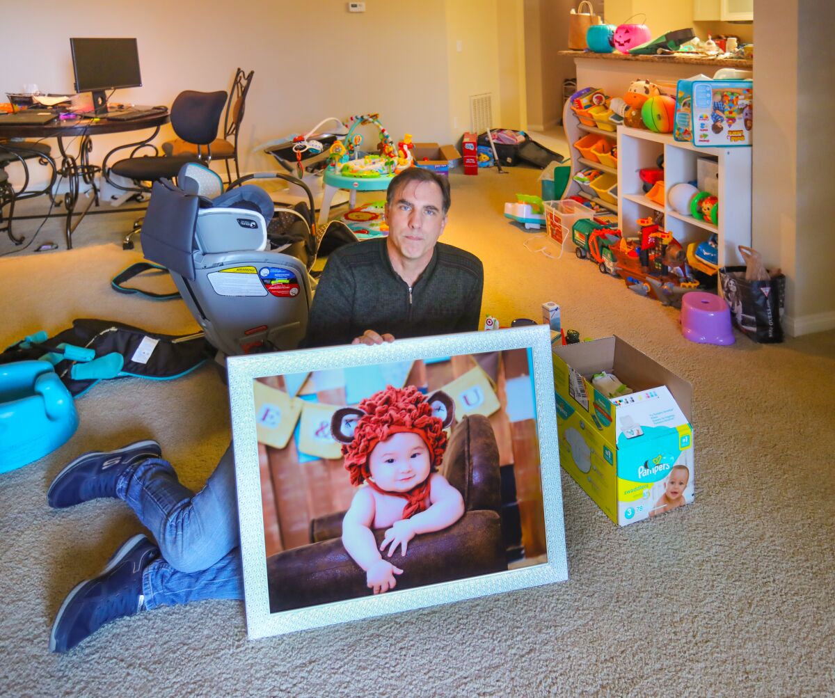 Ken Burnett sits in the living room of his Kearny Mesa apartment full of children's toys and other items they use, with a photo of his son, Rowan Burnett, 3, January 29, 2020 in San Diego, California. His wife, Ynjun Wei, son and daughter, Mia Burnett, 1, are all stuck in Wuhan, China, because of the Coronavirus outbreak. They have been there since November, and were planning on coming back to San Diego next week.