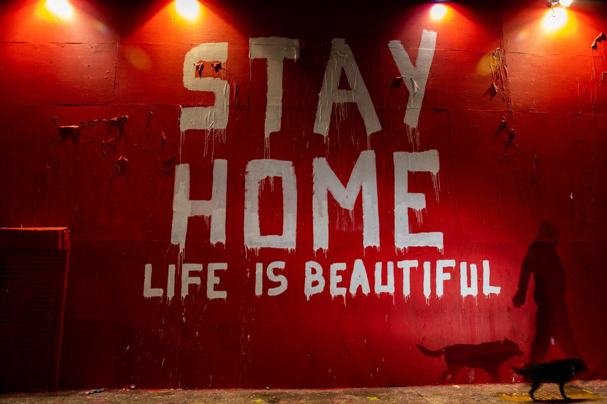 A man walks by a mural that says "Stay Home, Life is Beautiful."