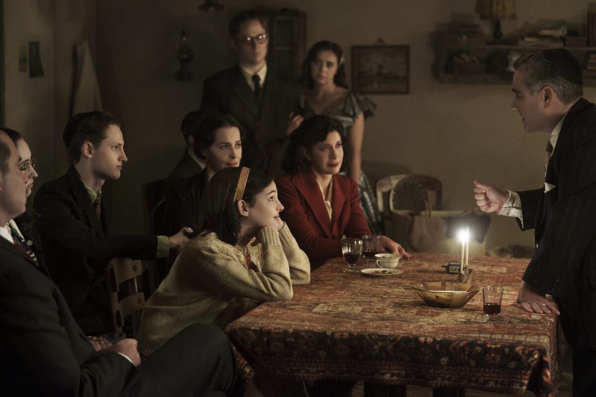 In a scene from "A Small Light," Jan and Miep Gies are at a table surrounded by people.