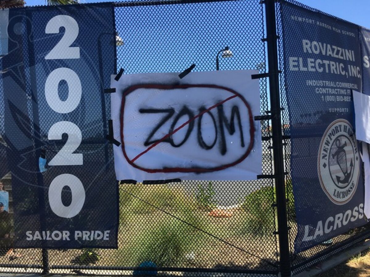 A sign taped to a fence at Newport Harbor High School has the word 'ZOOM' striked out. The Newport-Mesa Unified School District Board of Trustees voted Tuesday to cancel in-person graduations in June.