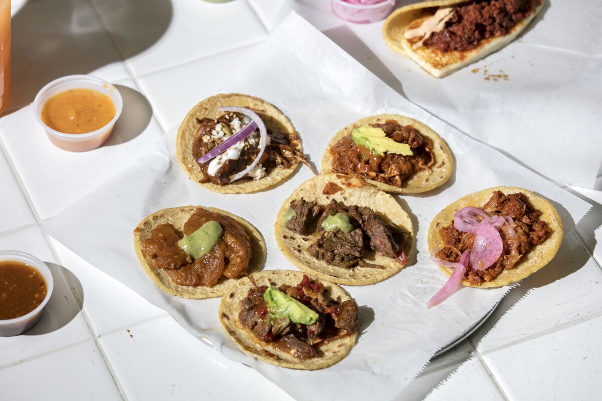 A circle of small Guisados tacos on a tray atop white tile.