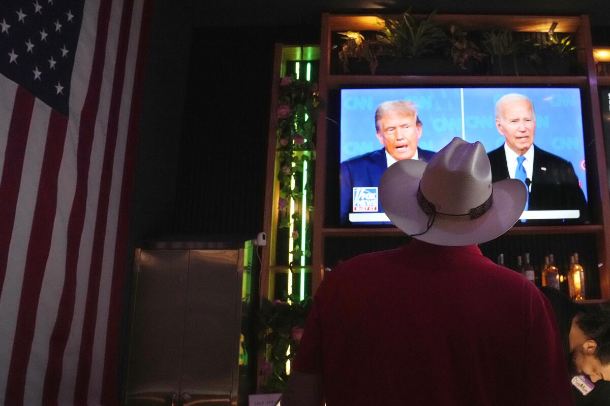 A man in a cowboy hat next to a U.S. flag watches the Biden-Trump debate