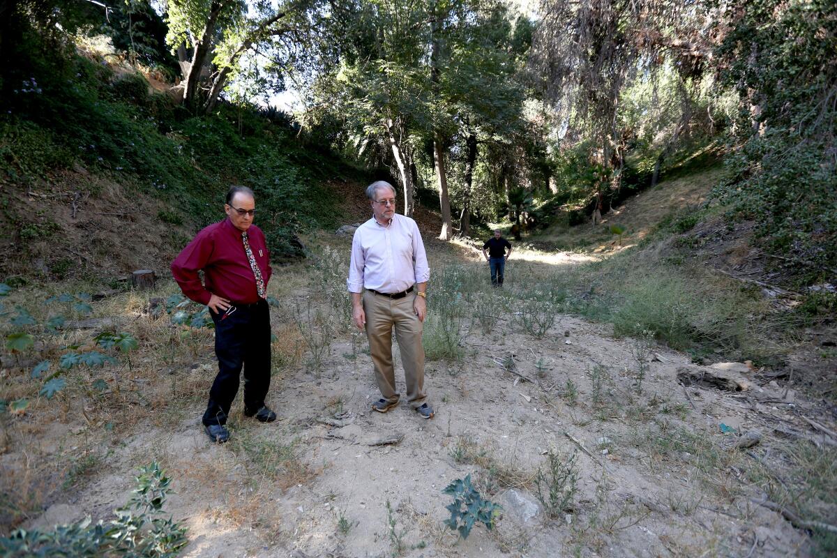 La Cañada Public Works director Pat DeChellis, left, and resident David Haxton stand in the natural canyon south of Lutheran Church in the Foothills, near where the city believes a burst water pipe underneath Foothill Boulevard caused the road to sink. The city and the Foothill Municipal Water District have legal claims against each other on who is at fault for the subsidence.