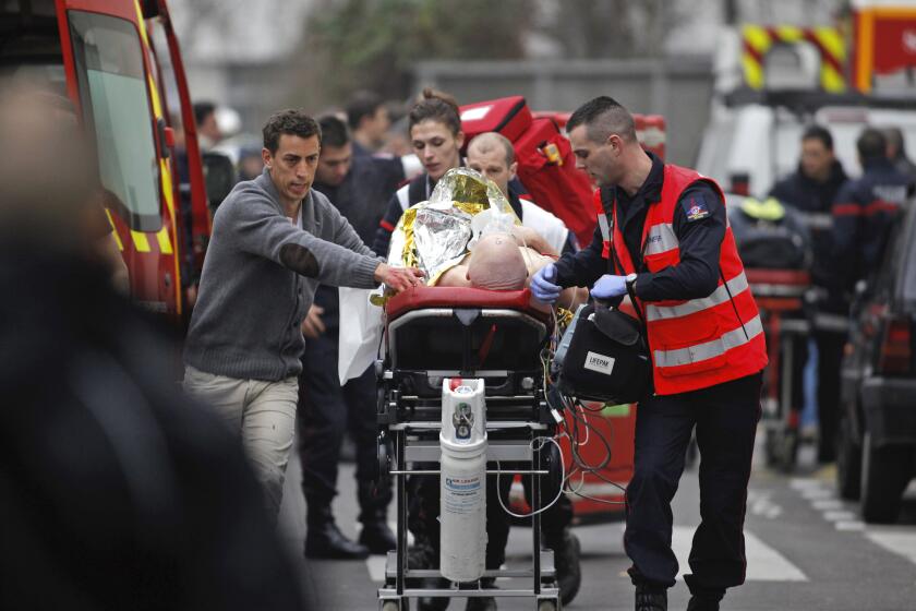 FILE - In this Jan. 7, 2015, file photo, an injured person is transported to an ambulance after a shooting at the French satirical newspaper Charlie Hebdo's office in Paris, France. The terrorism trial of 14 people linked to the January 2015 Paris attacks on the satirical weekly Charlie Hebdo and a kosher supermarket ends Wednesday after three months punctuated by new attacks, a wave of coronavirus infections among the defendants, and devastating testimony bearing witness to three days of bloodshed that shook France.(AP Photo/Thibault Camus, File)
