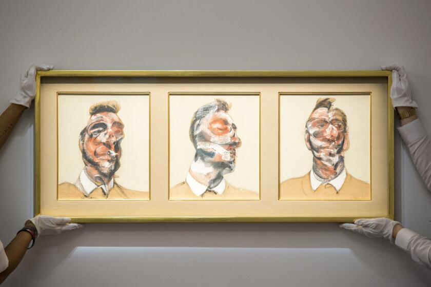 Art handlers hold Francis Bacon's 1964 piece "Three Studies for Portrait of George Dyer (on Light Ground)," which sold at a Sotheby's auction in London.