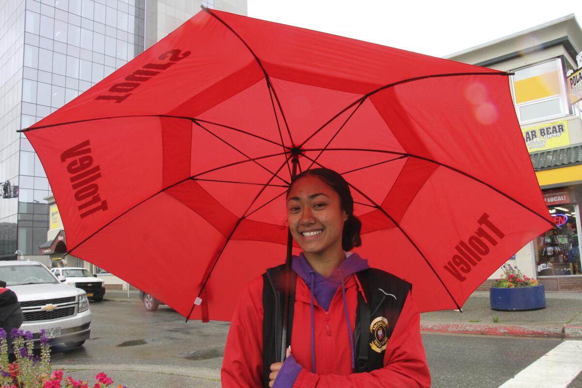A smiling young woman stands underneath her open red umbrella 