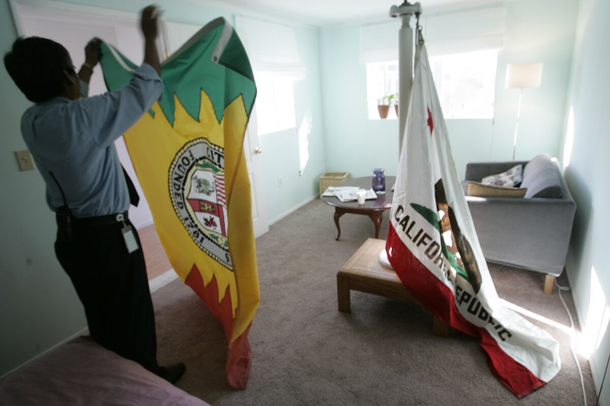 A man folds up the Los Angeles city flag in a room with the California state flag.