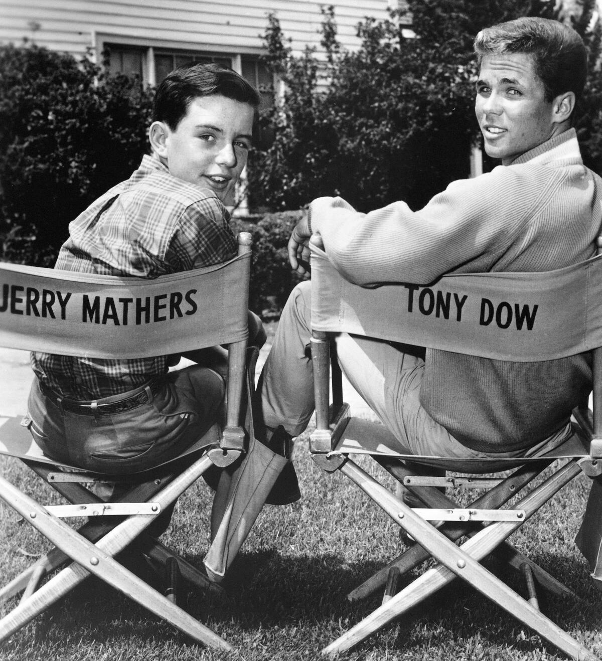 Two young men sitting in director's chairs and looking back at the camera.