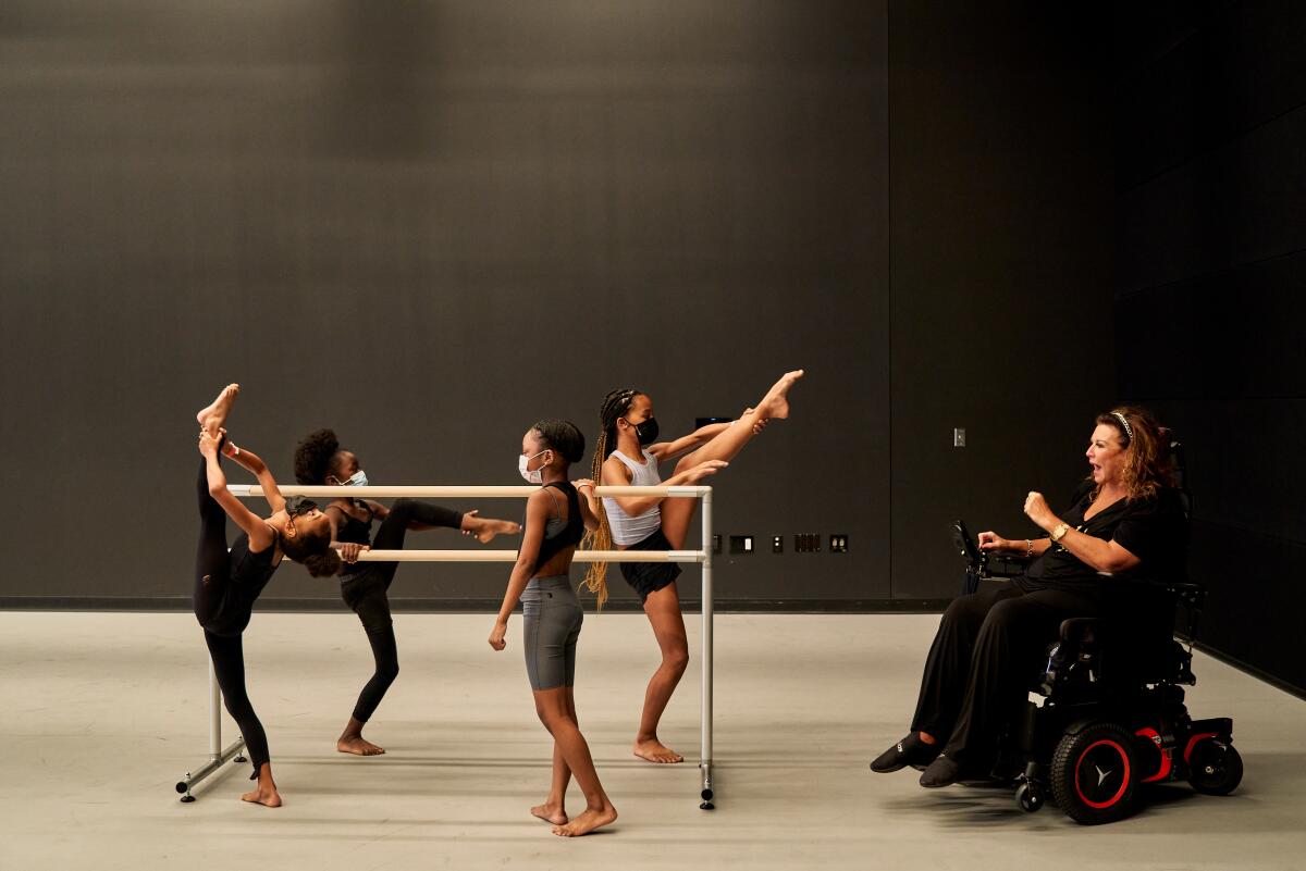 Children rehearse at a ballet barre while an instructor speaks to them. 