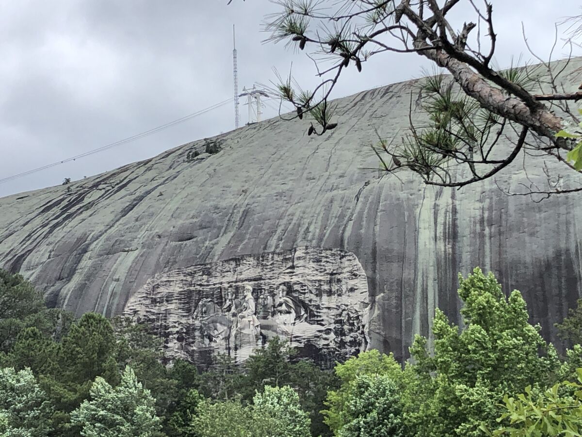 A bas-relief of Confederate leaders on horseback is carved into a massive outcropping of granite seen between tree branches.