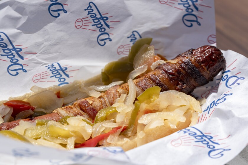 An extreme LA hot dog wrapped in bacon is located on the left plaza at the Think Blue BBQ restaurant at Dodger Stadium.