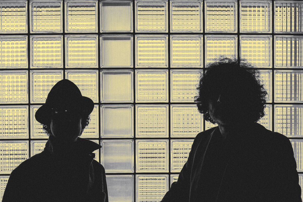two men backlit by glass tiles behind them