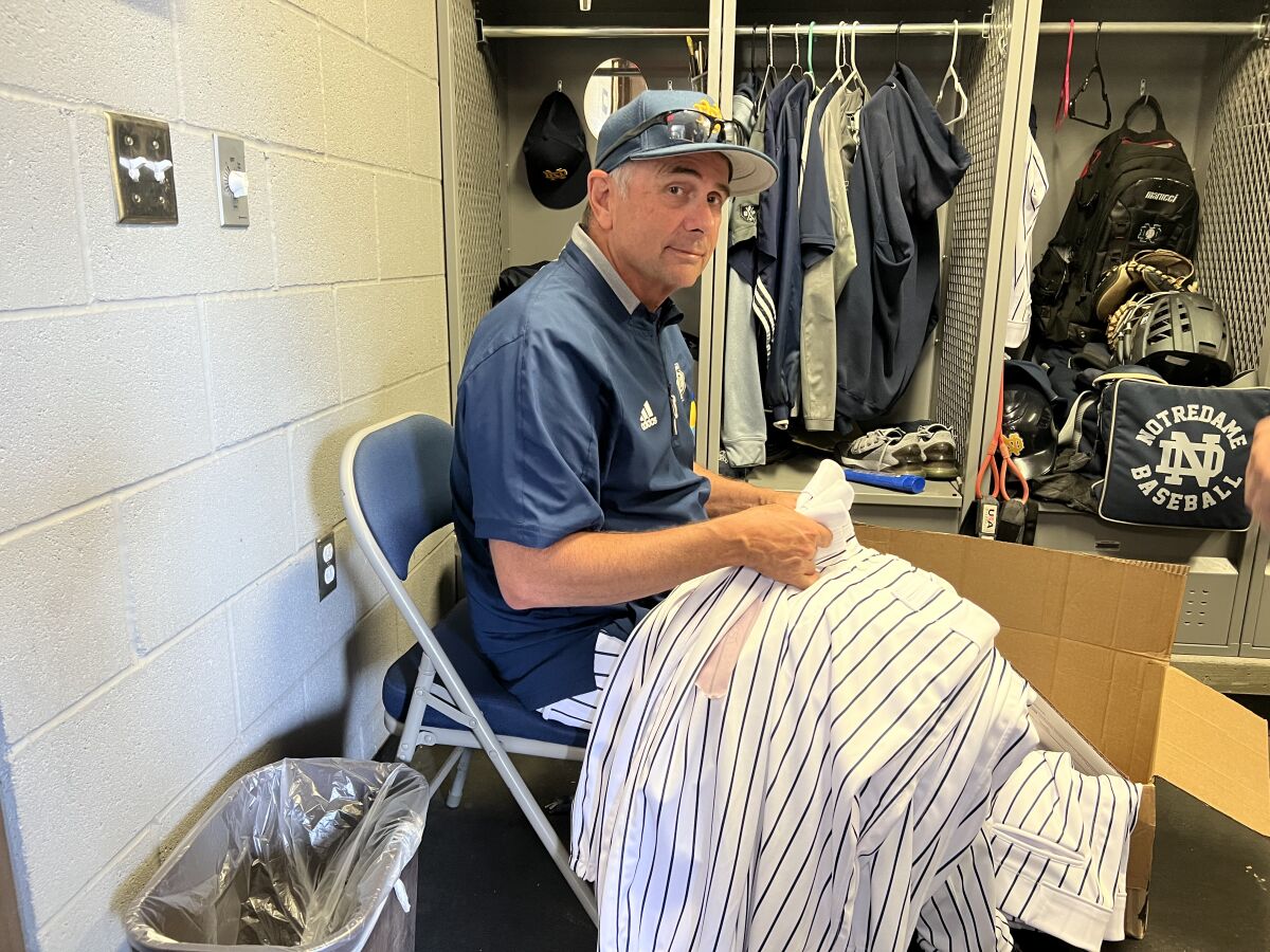 Coach Tom Dill sits in a folding chair with a pile of striped pants in his lap.